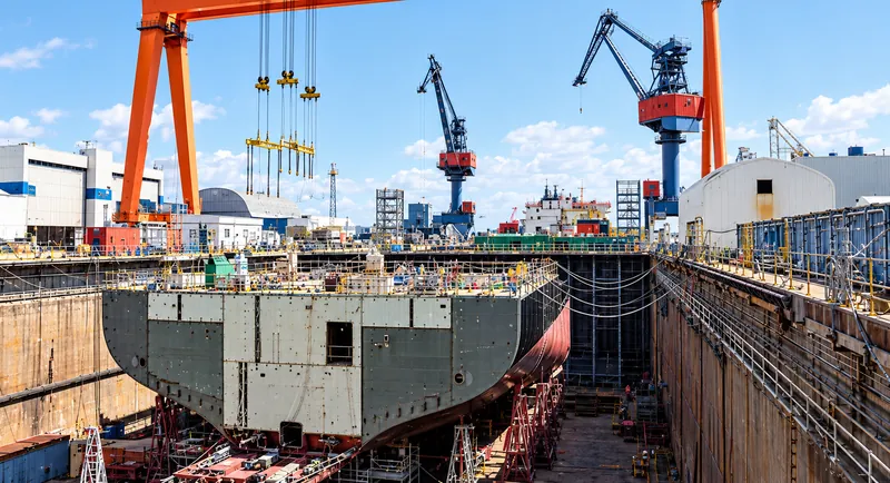 Defense infrastructure domain: warship in dry dock under gantry cranes